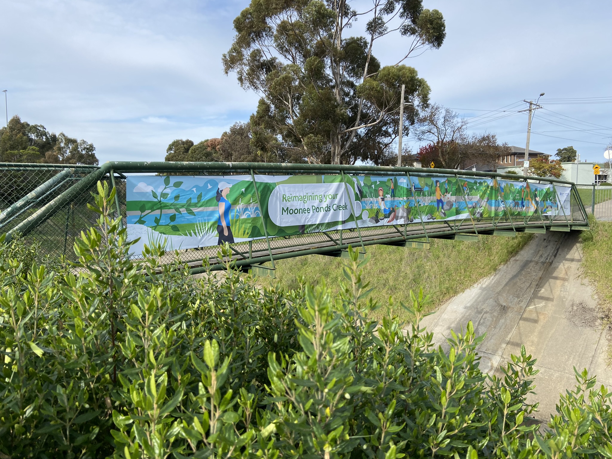 A banner across a bridge over the Moonee Ponds Creek reads Reimagining your Moonee Ponds Creek.