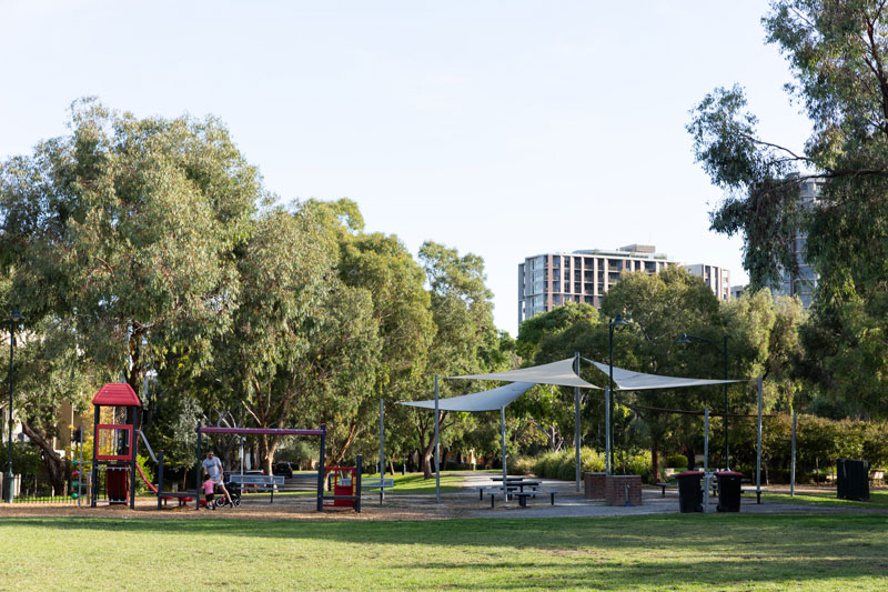 A playground and shaded BBQ and picnic area is seen from an open grassy space.