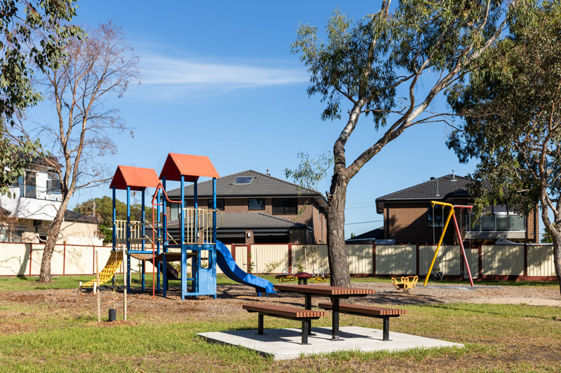 Colourful children's playground with climbing structures, slides and swings next to a picnic table.