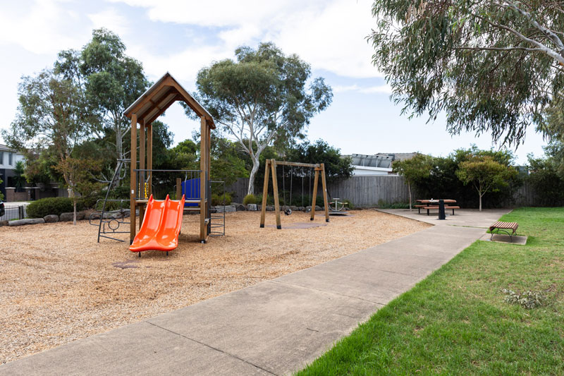 Children's playground with dual slides, swings and nearby seating and drink fountain.