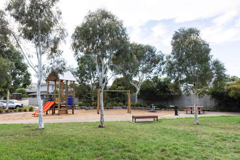 Children's playground area with nearby seating and drink fountain and native trees.