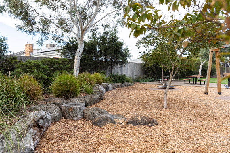 Landscaped area next to playground with logs. rocks and native vegetation.