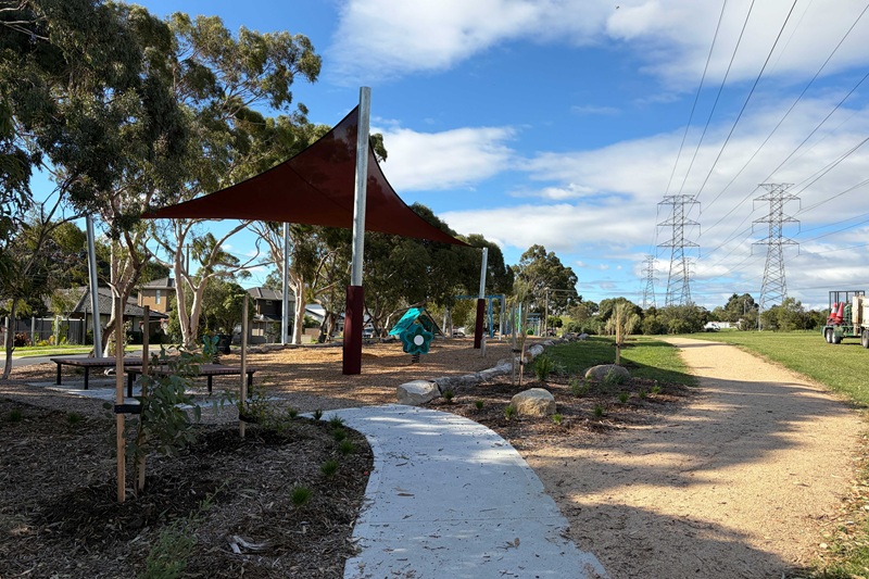 Shaded playground area with seating next to walking path.