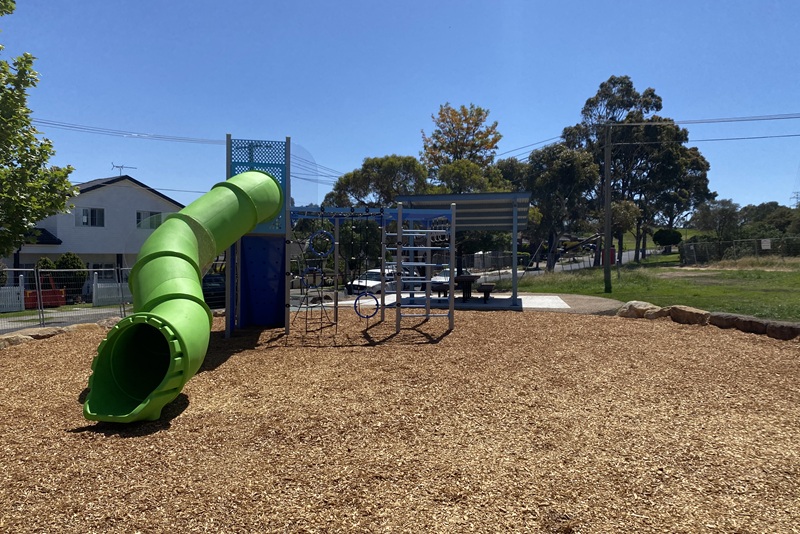 Children's playground with climbing structure and slide with undercover picnic table adjacent.