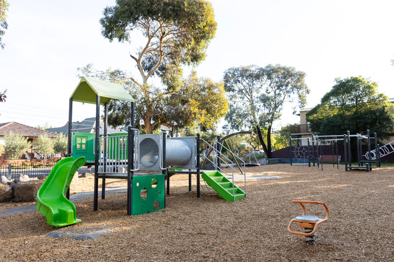 Bright green play equipment in this park includes slides and a tunnel in the foreground, with monkey bars and climbing frames in the background.