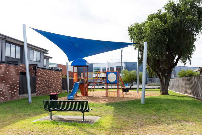 A small, shaded children's playground with a bench seat.