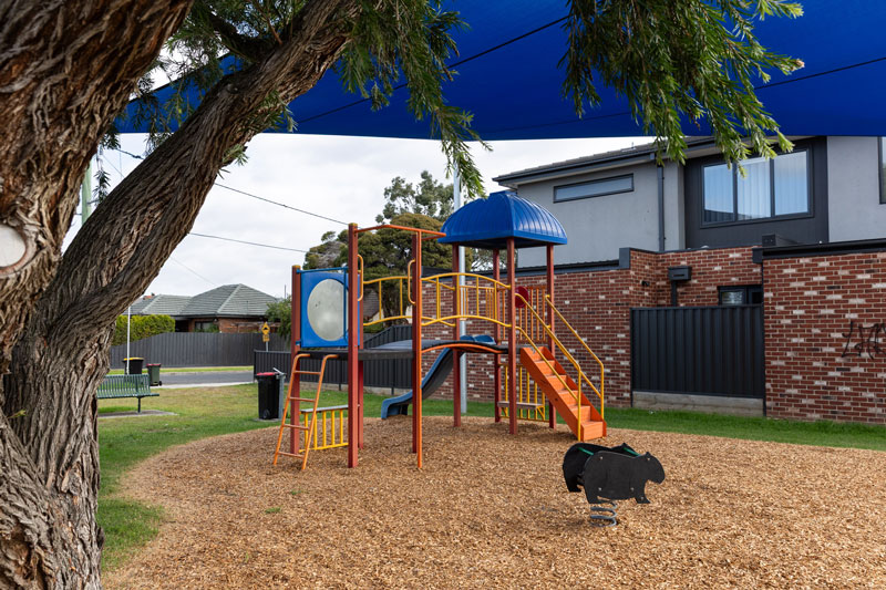 A small children's playground with climbing structures and slide with houses in the background.
