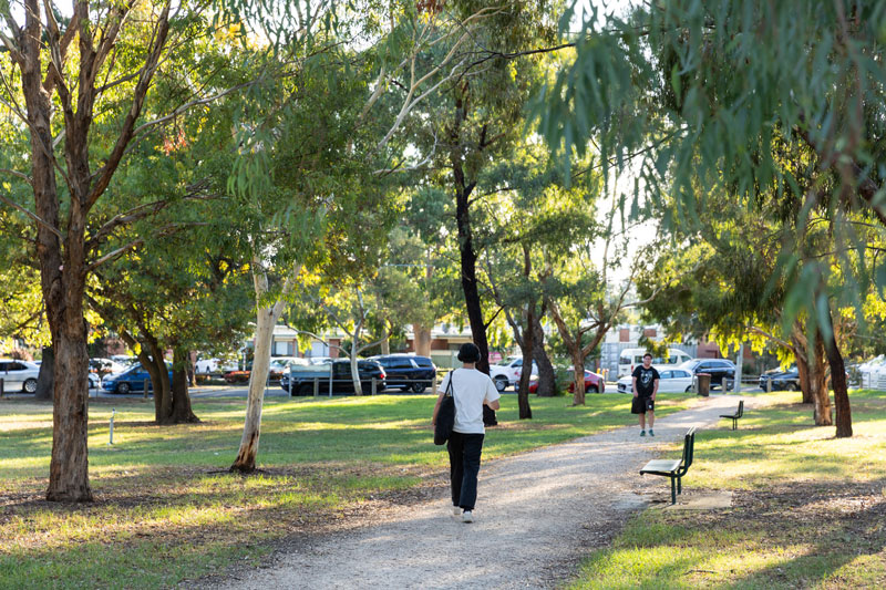 Two people walking along a path shaded by native trees.