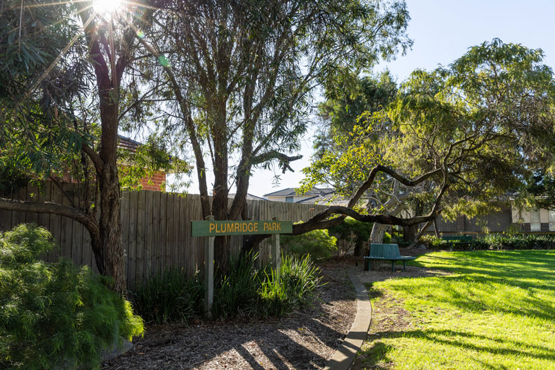 The Plumridge Park sign next the fence, flanked by native trees.