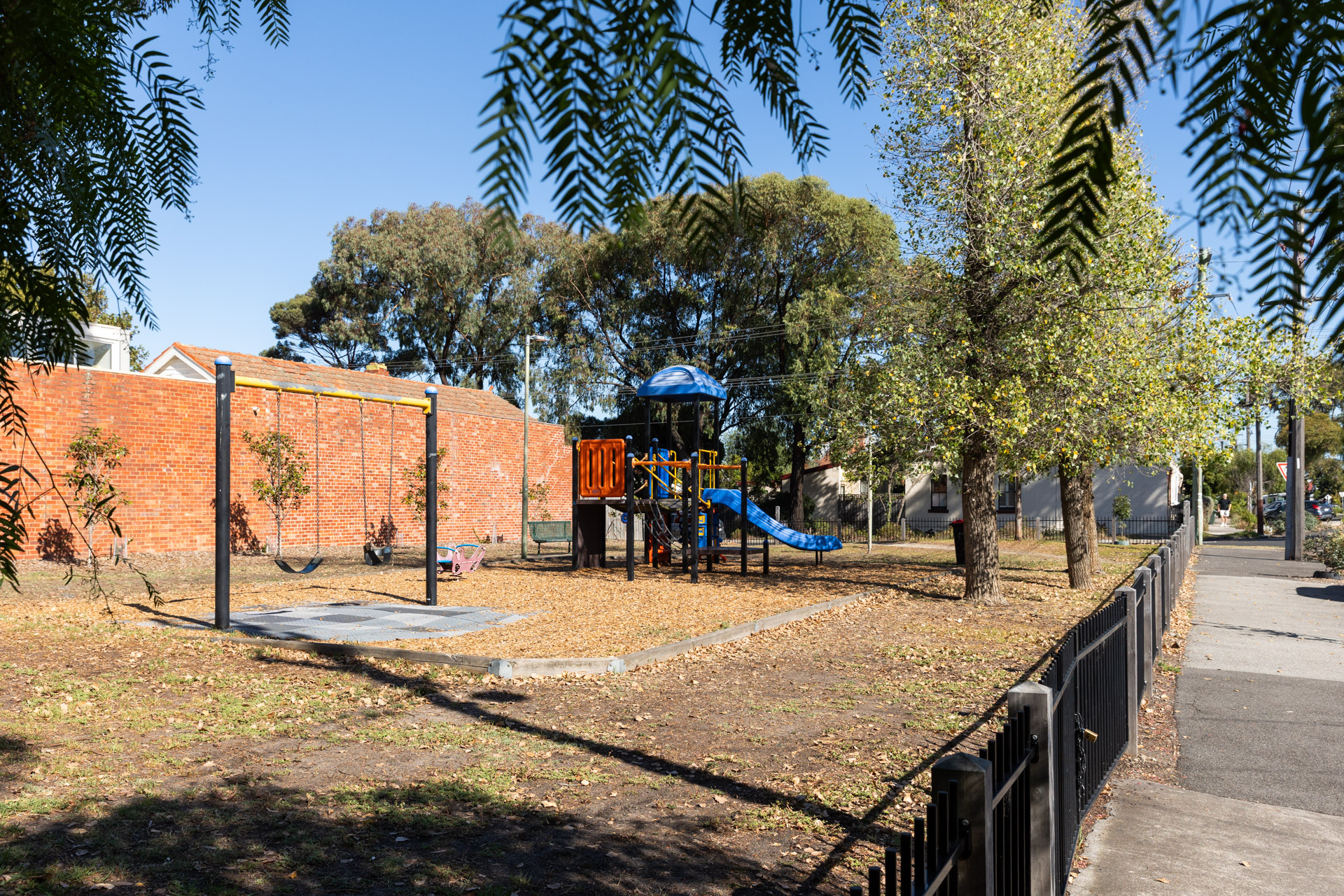A small fenced park with a colourful play tower and slide and small set of swings.