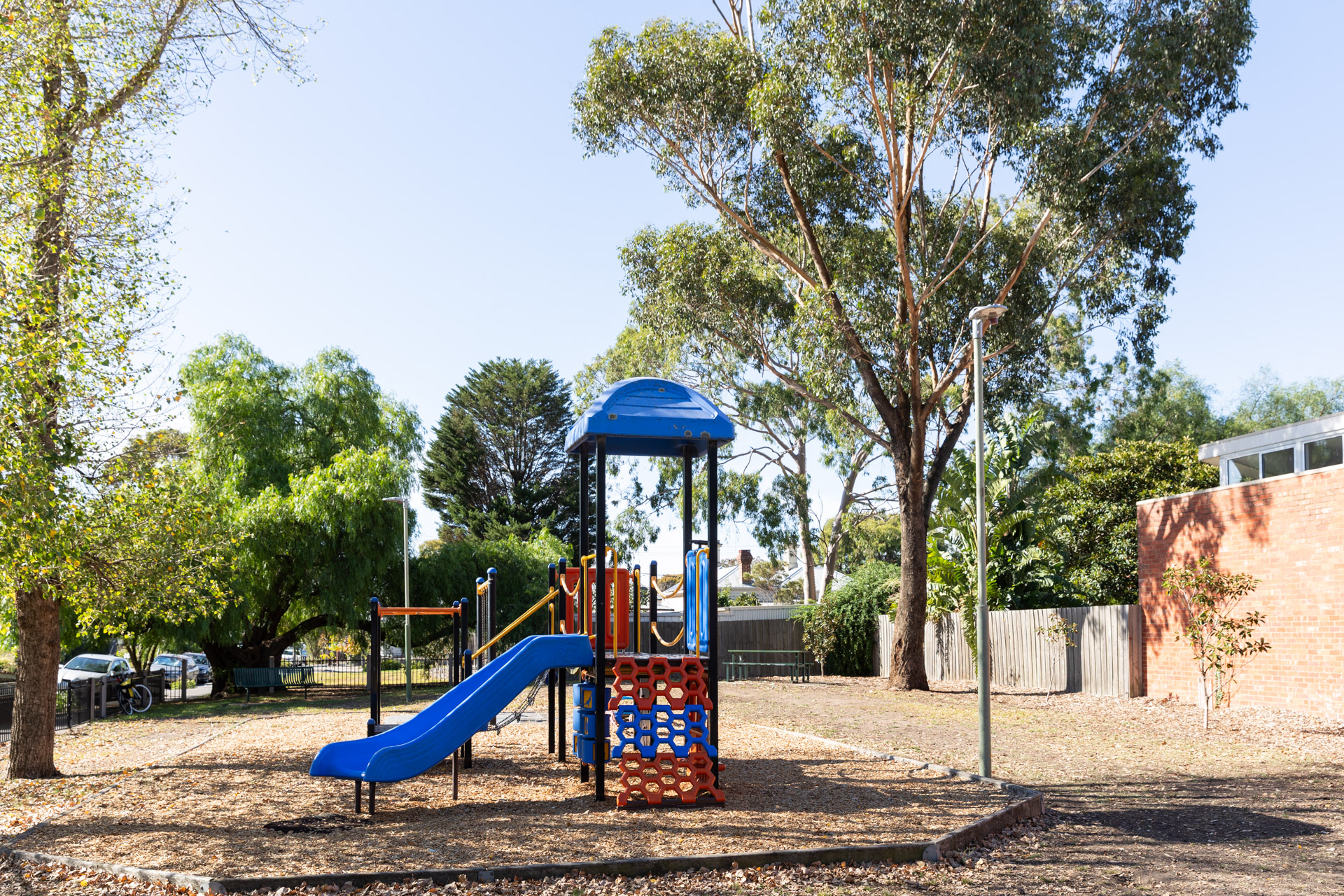 A primary coloured play tower with blue slide in a small fenced park,
