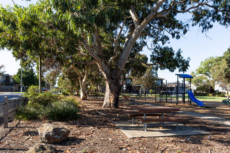 A picnic table with large native trees and a children's playground in the background.